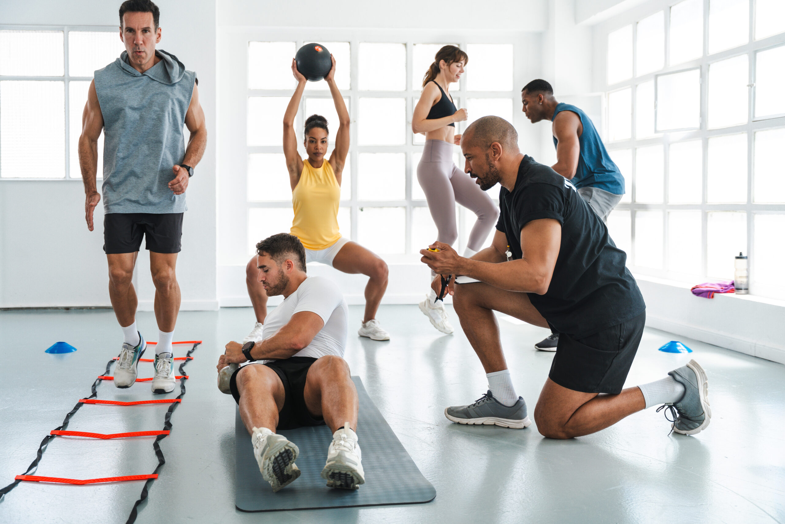 Multiethnic group of sportive people doing functional workout in training class gym diverse athletes exercising with a personal trainer in a bright. Modern gym